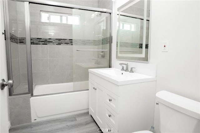 full bathroom featuring bath / shower combo with glass door, toilet, vanity, and hardwood / wood-style floors