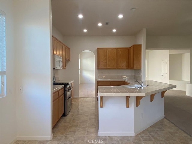 kitchen featuring double oven range, sink, kitchen peninsula, tile countertops, and a breakfast bar