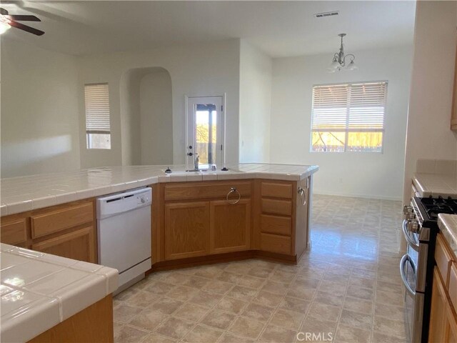 kitchen featuring tile countertops, white dishwasher, pendant lighting, and stainless steel gas range oven