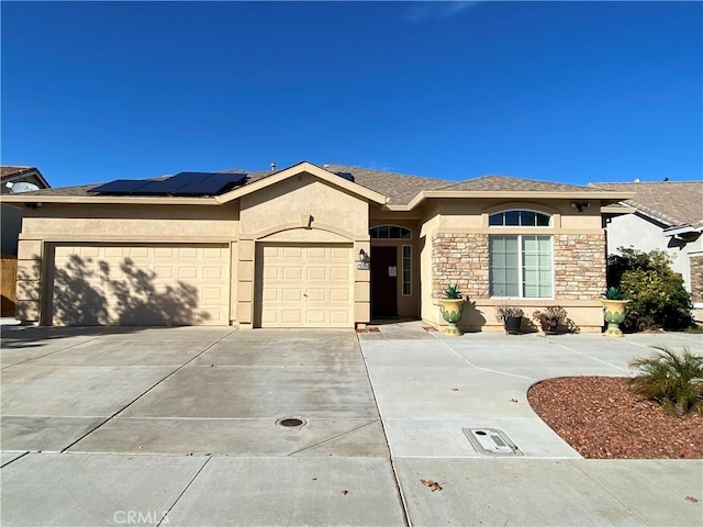 single story home with an attached garage, solar panels, stone siding, driveway, and stucco siding