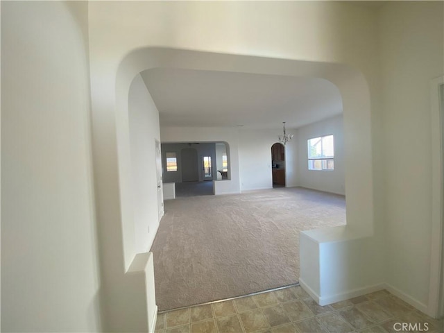 unfurnished living room featuring baseboards, arched walkways, a chandelier, and light colored carpet