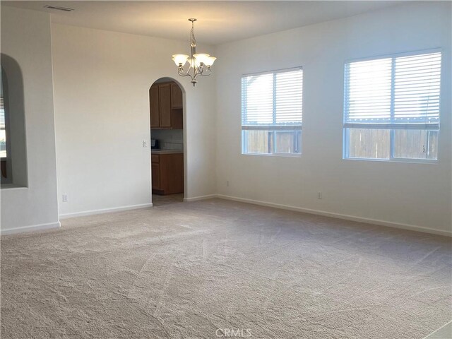 carpeted spare room featuring an inviting chandelier