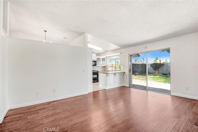 unfurnished living room featuring vaulted ceiling, a textured ceiling, and hardwood / wood-style flooring