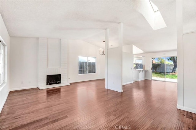 unfurnished living room with a brick fireplace, hardwood / wood-style flooring, lofted ceiling with skylight, and a notable chandelier