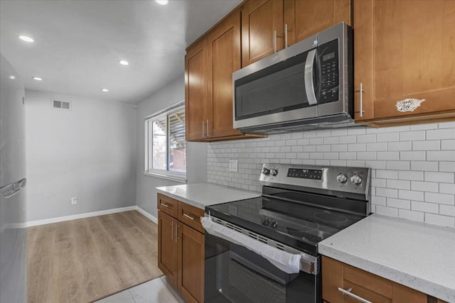 kitchen with stainless steel appliances, decorative backsplash, light hardwood / wood-style flooring, and light stone counters