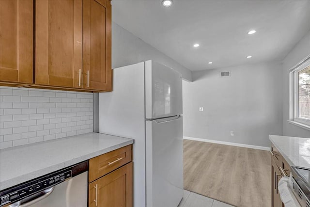 kitchen with tasteful backsplash, dishwasher, light hardwood / wood-style flooring, light stone countertops, and white refrigerator