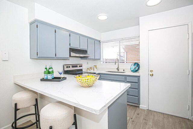 kitchen with sink, light hardwood / wood-style flooring, stainless steel range with electric stovetop, a kitchen breakfast bar, and kitchen peninsula