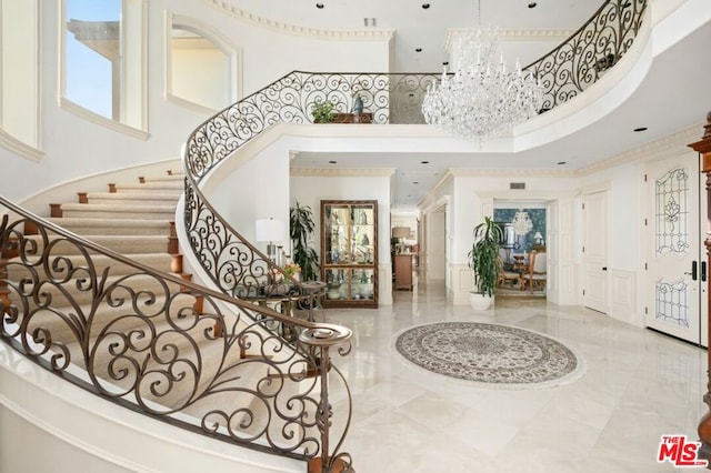 entrance foyer with a towering ceiling, ornamental molding, and a notable chandelier