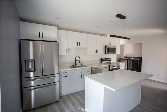 kitchen with hanging light fixtures, appliances with stainless steel finishes, white cabinets, a sink, and washer and dryer