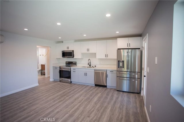 kitchen featuring light countertops, appliances with stainless steel finishes, white cabinets, a sink, and baseboards