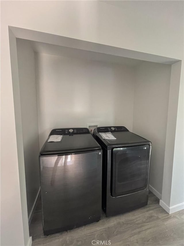 clothes washing area featuring baseboards, laundry area, light wood-style flooring, and washer and dryer