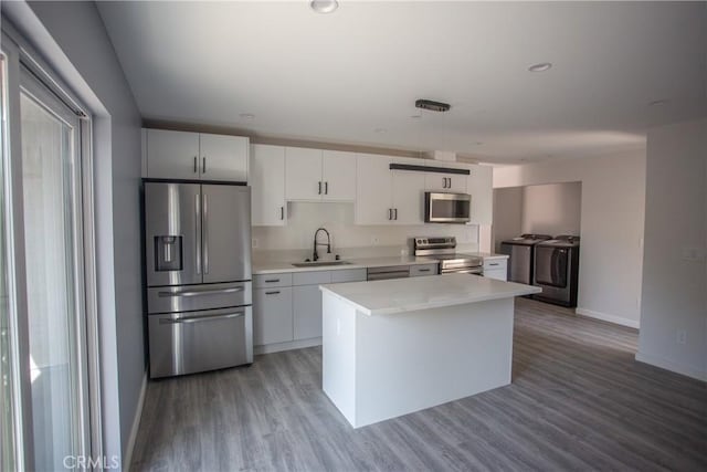 kitchen featuring washer and clothes dryer, appliances with stainless steel finishes, light countertops, white cabinetry, and a sink