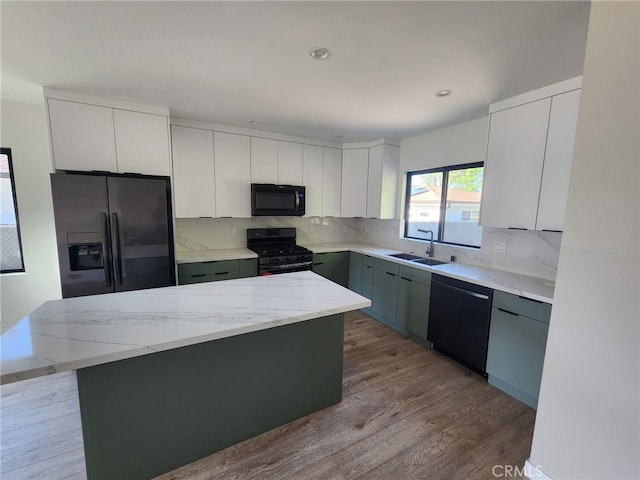 kitchen featuring decorative backsplash, white cabinets, a kitchen island, black appliances, and a sink