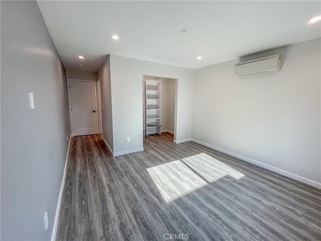 unfurnished bedroom with recessed lighting, baseboards, an AC wall unit, and wood finished floors