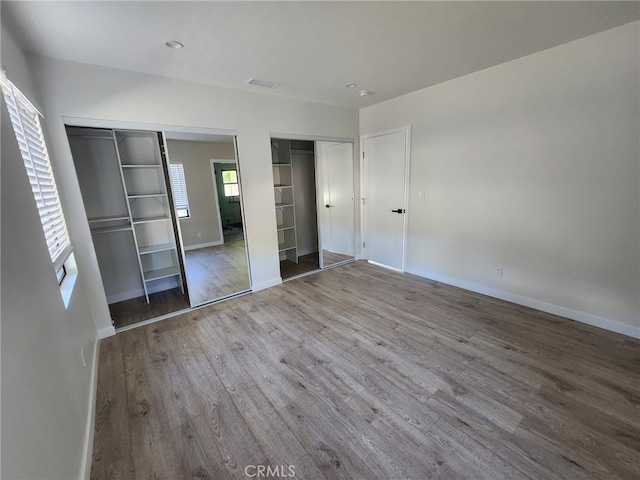 unfurnished bedroom with wood finished floors, visible vents, baseboards, and two closets