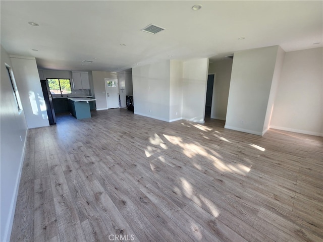 unfurnished living room featuring visible vents, light wood-style flooring, and baseboards