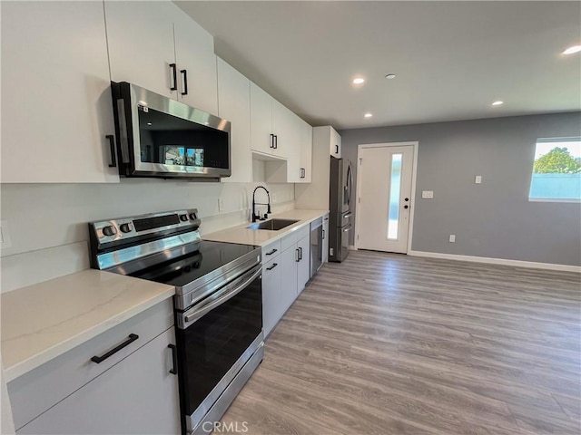 kitchen with light stone countertops, stainless steel appliances, light wood-type flooring, white cabinetry, and a sink