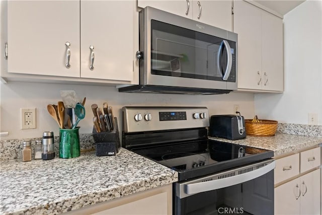 kitchen with light stone countertops, stainless steel appliances, and white cabinetry