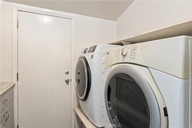 clothes washing area with washer and clothes dryer and cabinets