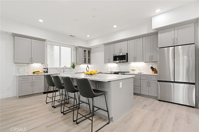 kitchen with a kitchen island, appliances with stainless steel finishes, light wood-type flooring, and a kitchen bar