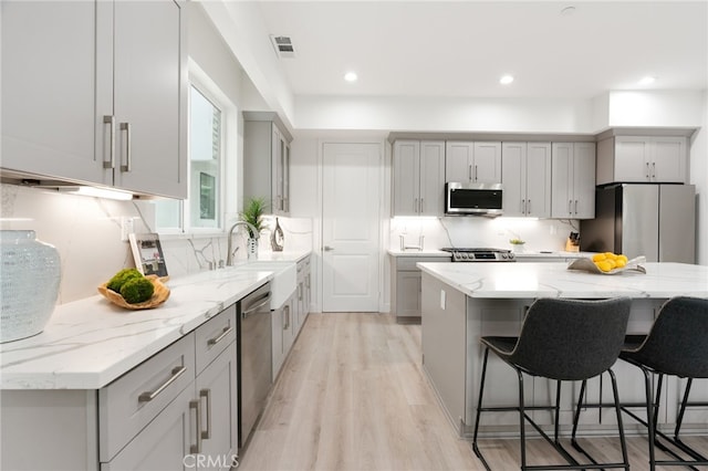 kitchen with sink, light hardwood / wood-style flooring, appliances with stainless steel finishes, gray cabinets, and light stone countertops