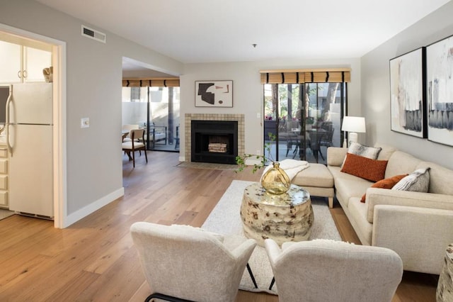 living room featuring a tiled fireplace and light wood-type flooring