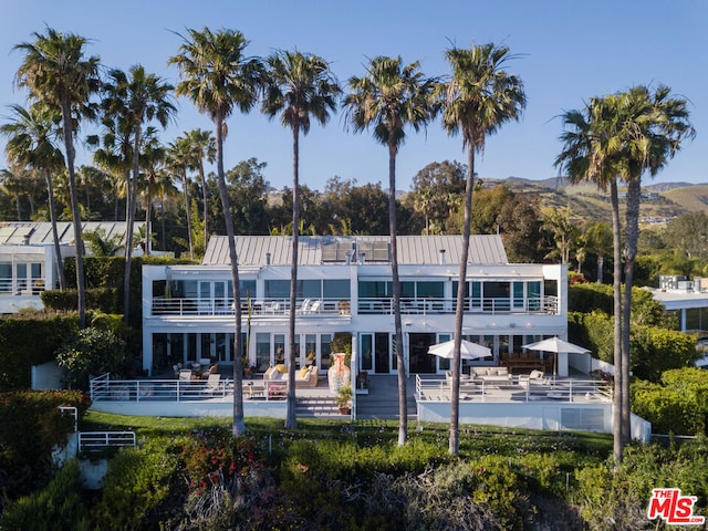 rear view of house with a patio area, a pool, a mountain view, and a balcony