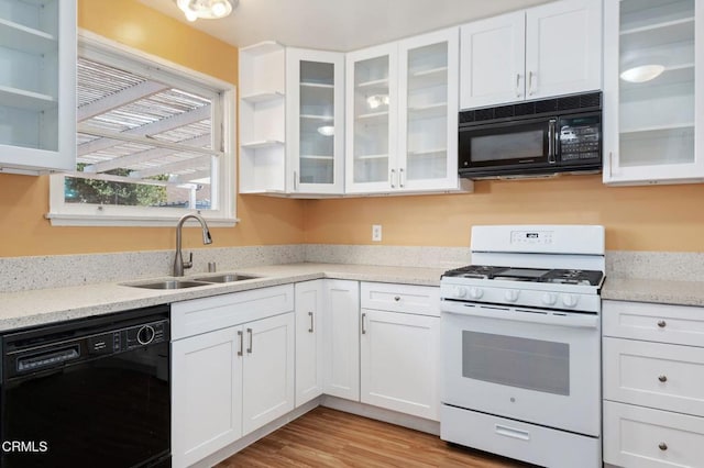 kitchen with light stone countertops, white cabinets, black appliances, sink, and light wood-type flooring