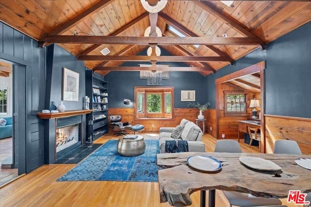 living room featuring wood-type flooring, wood walls, and vaulted ceiling with beams