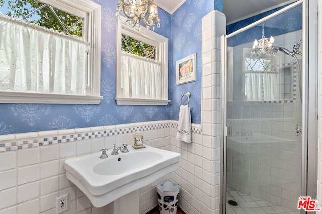 bathroom featuring an inviting chandelier, sink, a shower with shower door, and tile walls