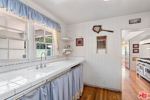 kitchen featuring sink, high quality appliances, tile counters, ornamental molding, and hardwood / wood-style floors