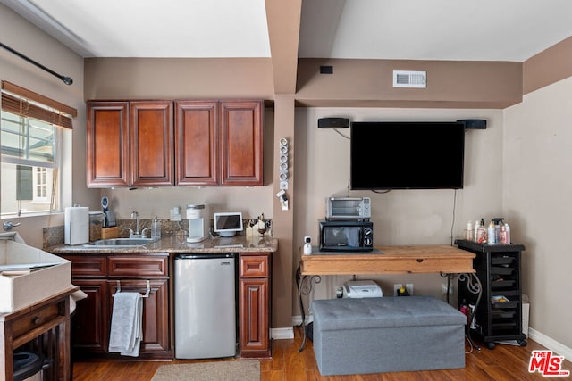 kitchen with hardwood / wood-style flooring, light stone countertops, sink, and stainless steel fridge