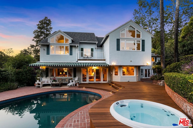 back house at dusk featuring outdoor lounge area, a balcony, a hot tub, and a deck