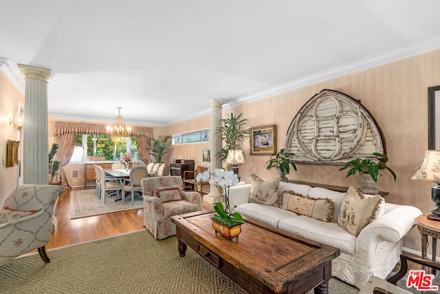 living room featuring decorative columns, wood-type flooring, ornamental molding, and a chandelier