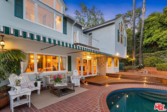 pool at dusk with a wooden deck and a patio