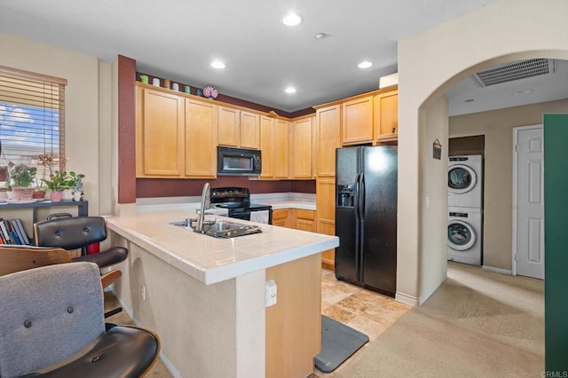 kitchen featuring stacked washer and clothes dryer, kitchen peninsula, tile counters, light brown cabinets, and black appliances