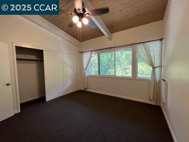 unfurnished bedroom featuring wooden ceiling, dark carpet, a closet, ceiling fan, and lofted ceiling with beams