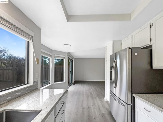 kitchen with stainless steel refrigerator with ice dispenser, light stone counters, white cabinetry, and light hardwood / wood-style flooring