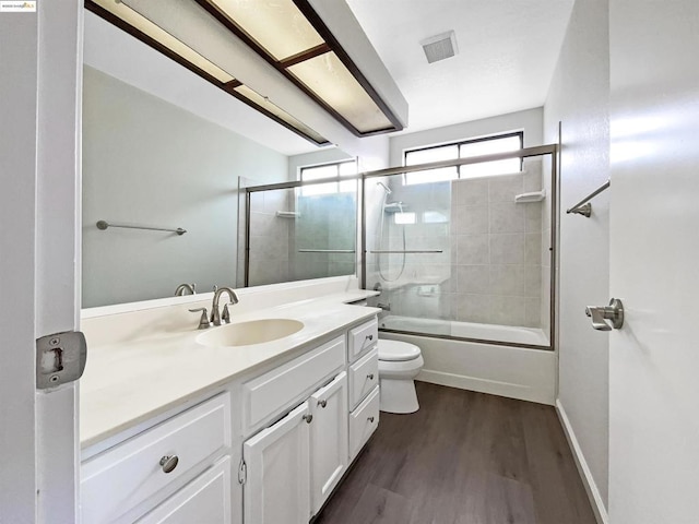 full bathroom with wood-type flooring, bath / shower combo with glass door, toilet, and vanity