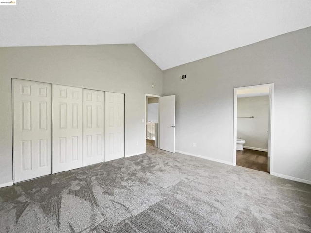 unfurnished bedroom with high vaulted ceiling, dark carpet, a closet, and ensuite bath