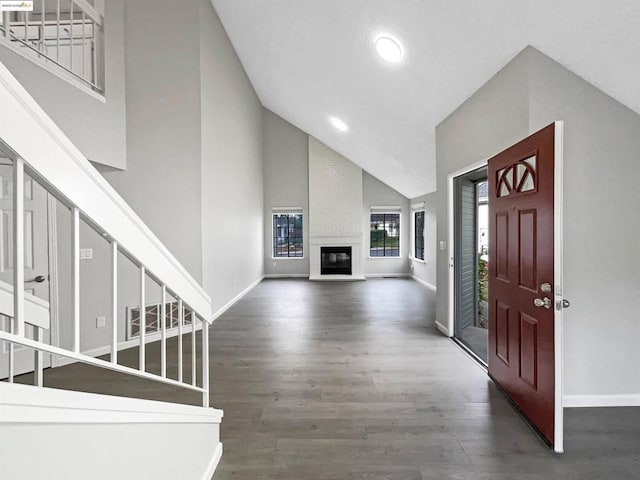 foyer entrance featuring a fireplace, dark wood-type flooring, and high vaulted ceiling