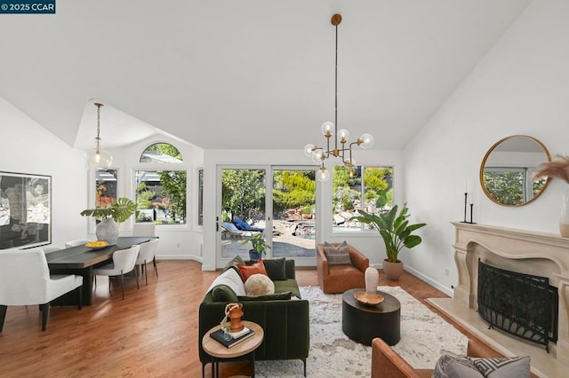 living room featuring a premium fireplace, wood-type flooring, lofted ceiling, and a notable chandelier