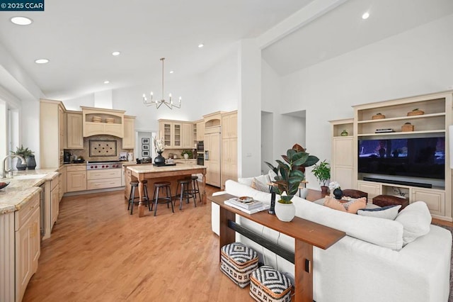 living room with an inviting chandelier, sink, light hardwood / wood-style floors, and high vaulted ceiling