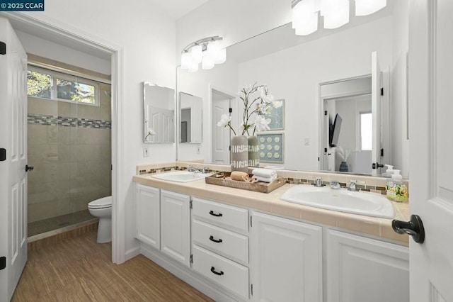 bathroom featuring hardwood / wood-style flooring, vanity, a tile shower, and toilet