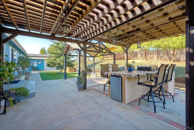 view of patio with area for grilling, a pergola, and exterior bar