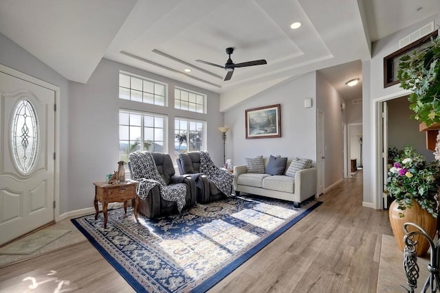 living room featuring ceiling fan, a tray ceiling, and light wood-type flooring