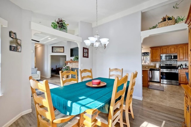 dining space featuring a stone fireplace, a towering ceiling, a notable chandelier, and light hardwood / wood-style flooring