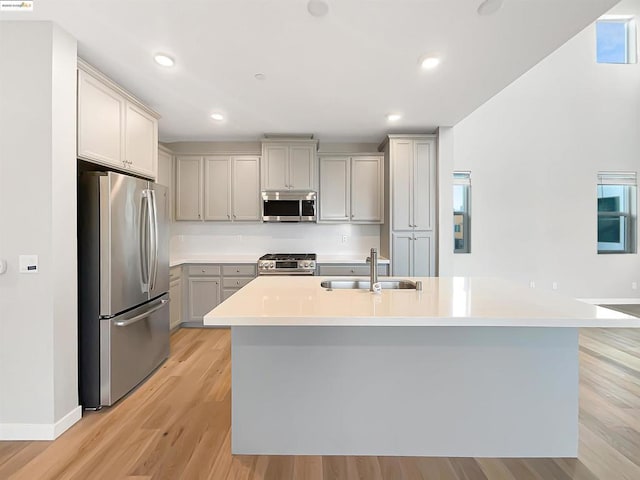 kitchen featuring appliances with stainless steel finishes, gray cabinetry, an island with sink, sink, and light hardwood / wood-style flooring