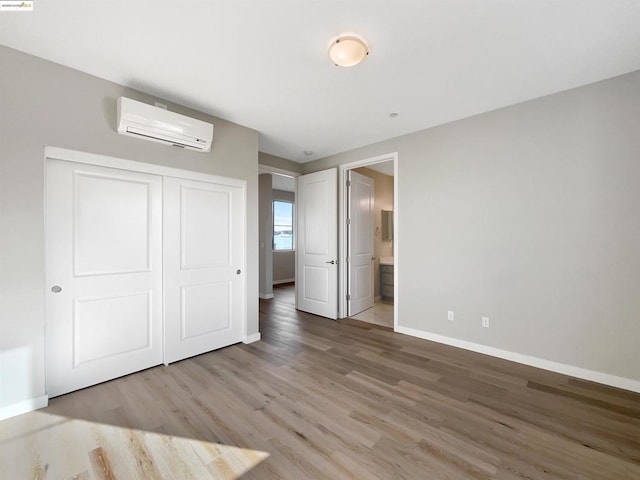 unfurnished bedroom featuring light hardwood / wood-style floors, connected bathroom, a closet, and a wall mounted air conditioner