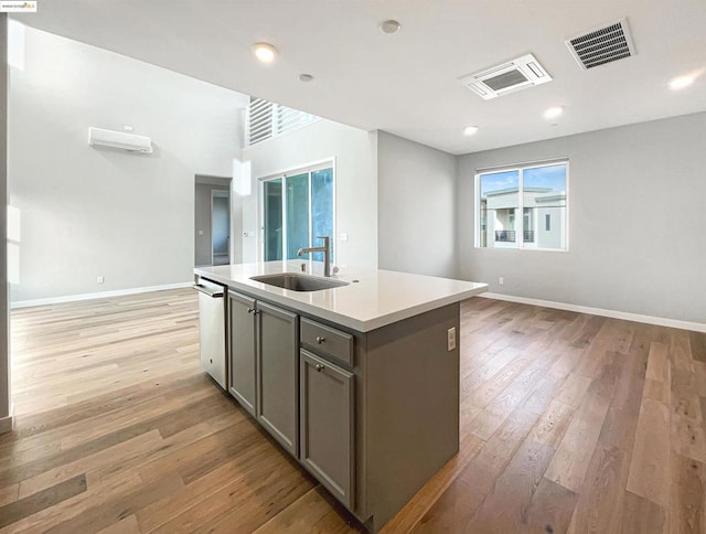 kitchen with dishwasher, sink, gray cabinets, an island with sink, and light hardwood / wood-style floors